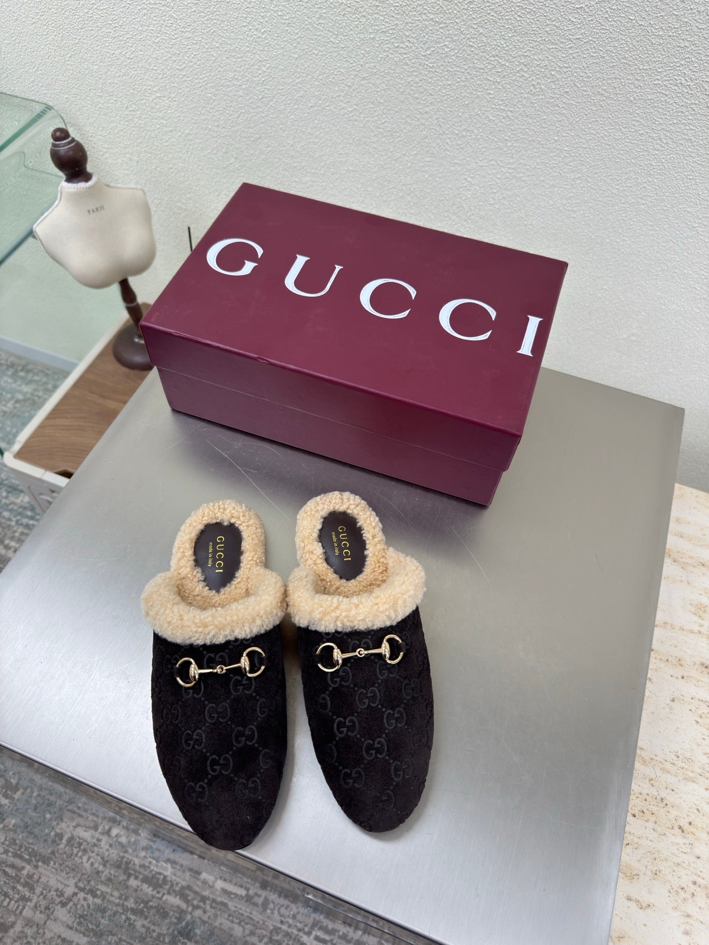 Gucci women’s slippers with dark textured upper, tan shearling lining, gold bit detail