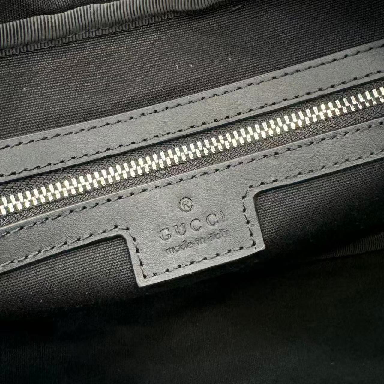 Gucci interior label on dark lining with stitching and zip pocket detail.