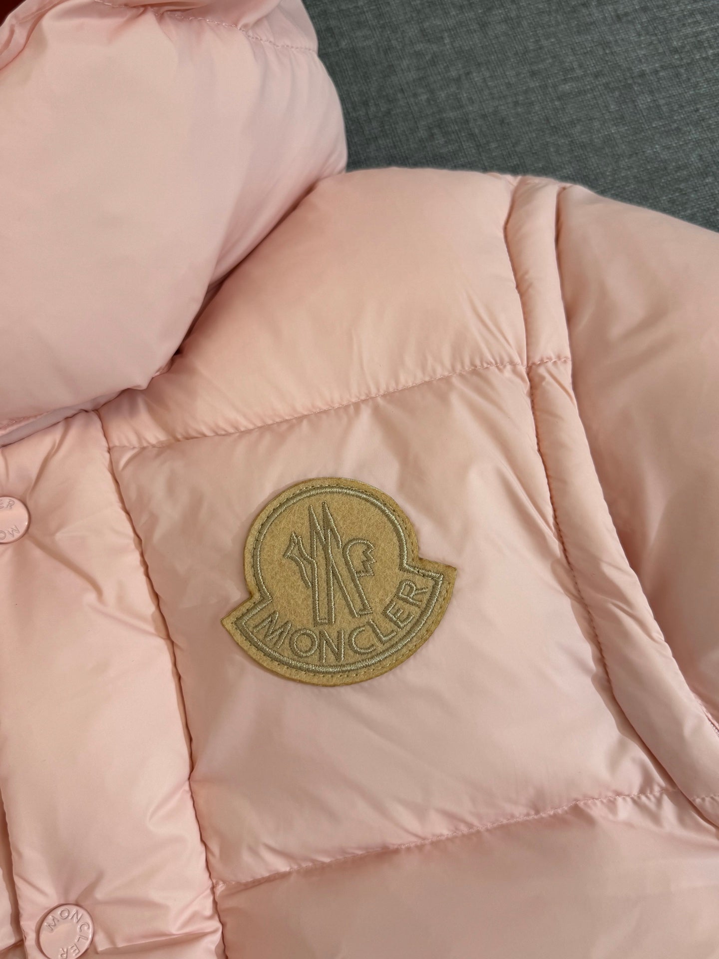 Moncler long puffer jacket, close-up of gold logo patch on pink quilted panel