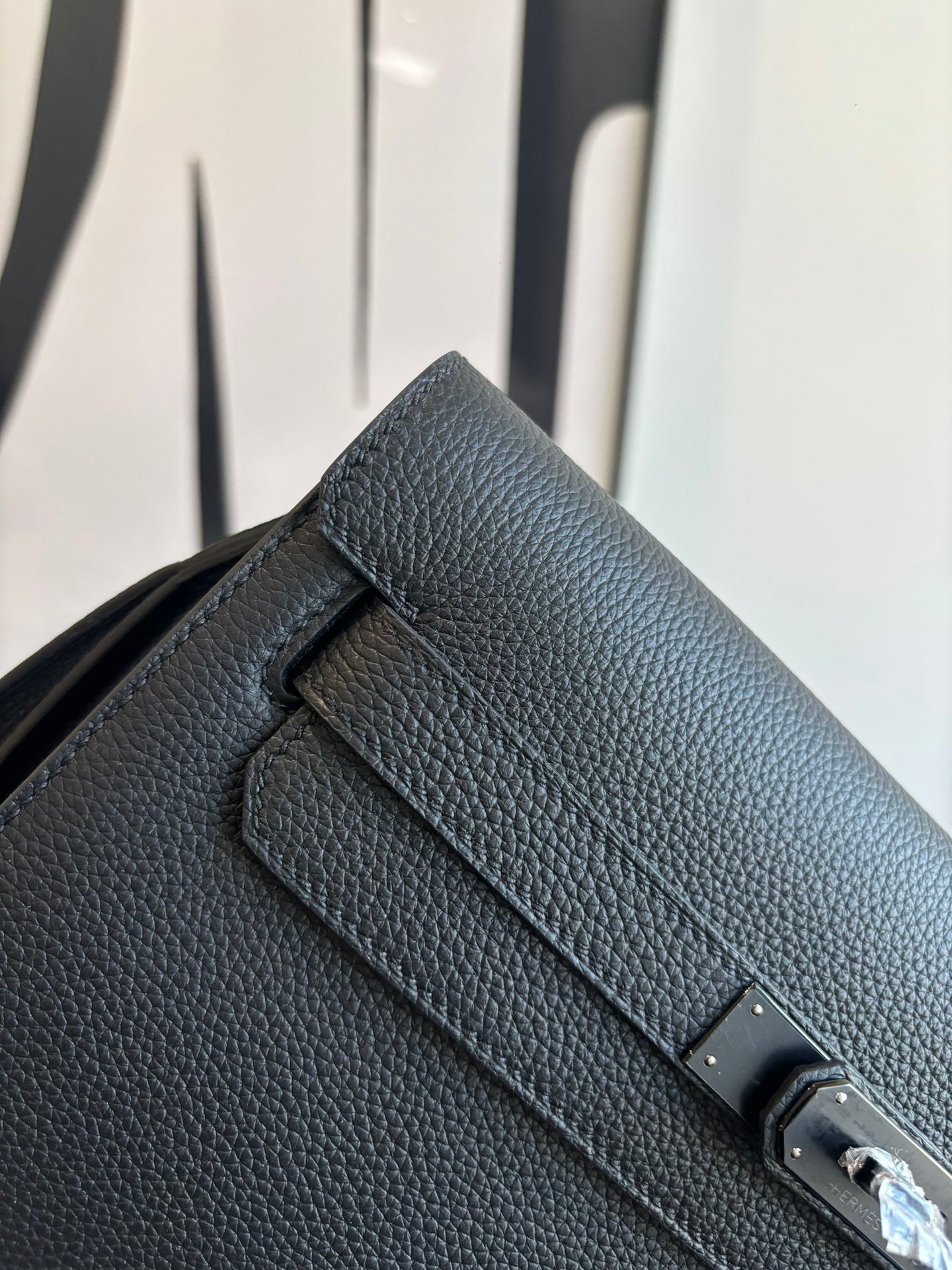 Hermes leather flap bag close-up of front strap tab and metal lock, textured dark grain