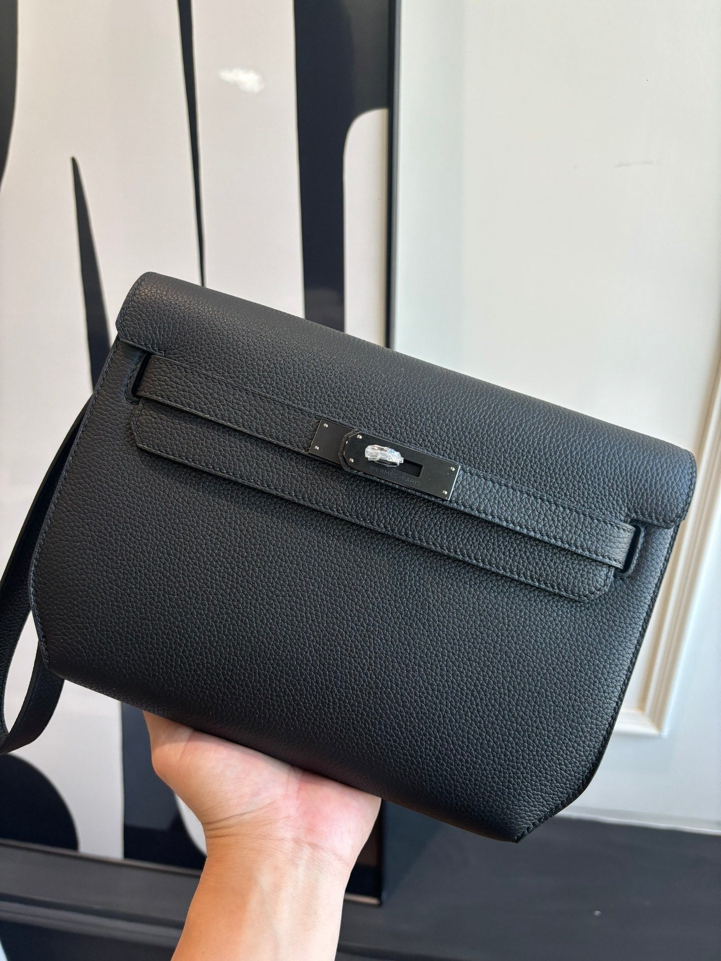 Hermes leather flap bag with front buckle clasp, textured dark grain finish, wrist strap