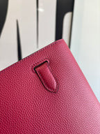 Hermes bag close-up of front flap edge with black-lined tab and textured red leather.