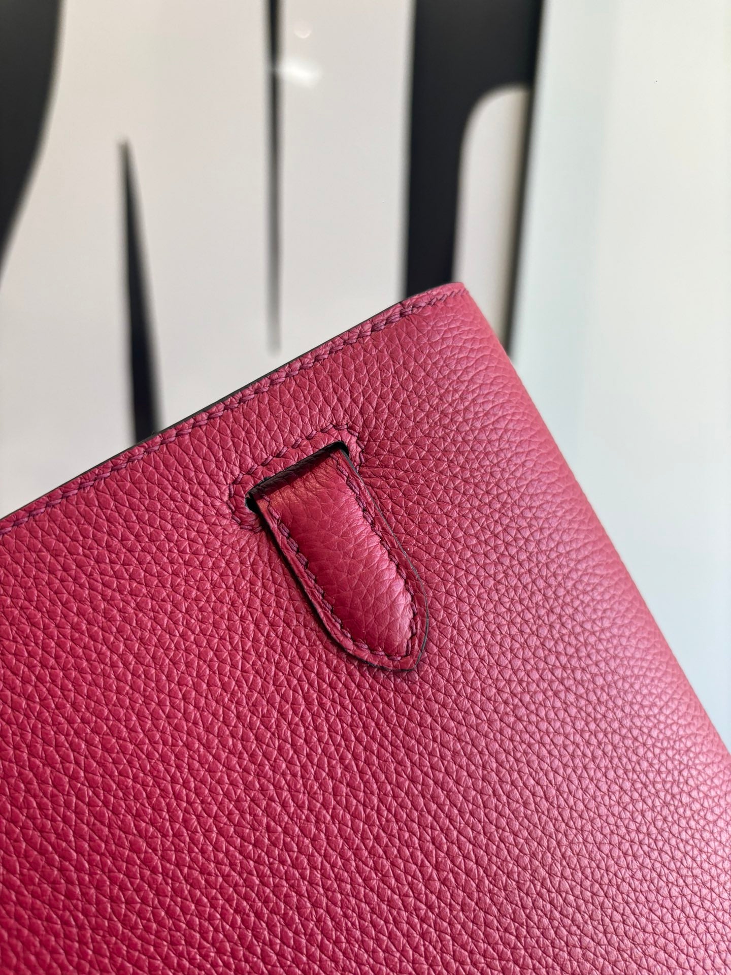 Hermes bag close-up of front flap edge with black-lined tab and textured red leather.