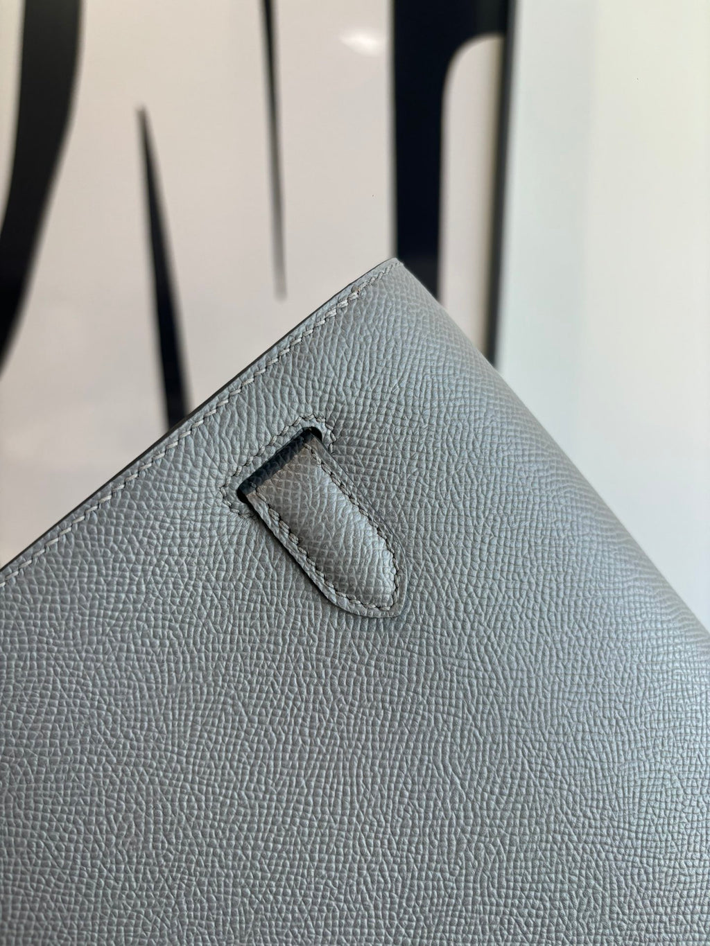 Hermes bag close-up of front flap tab on light blue-gray textured leather