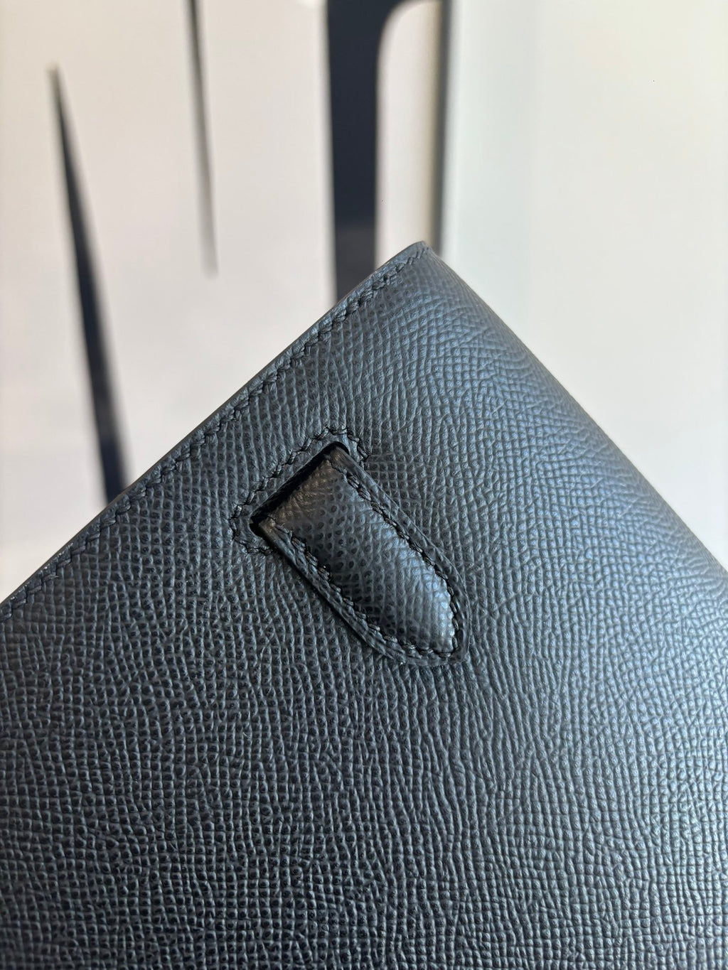 Flap bag corner close-up with stitched handle loop on textured dark blue leather