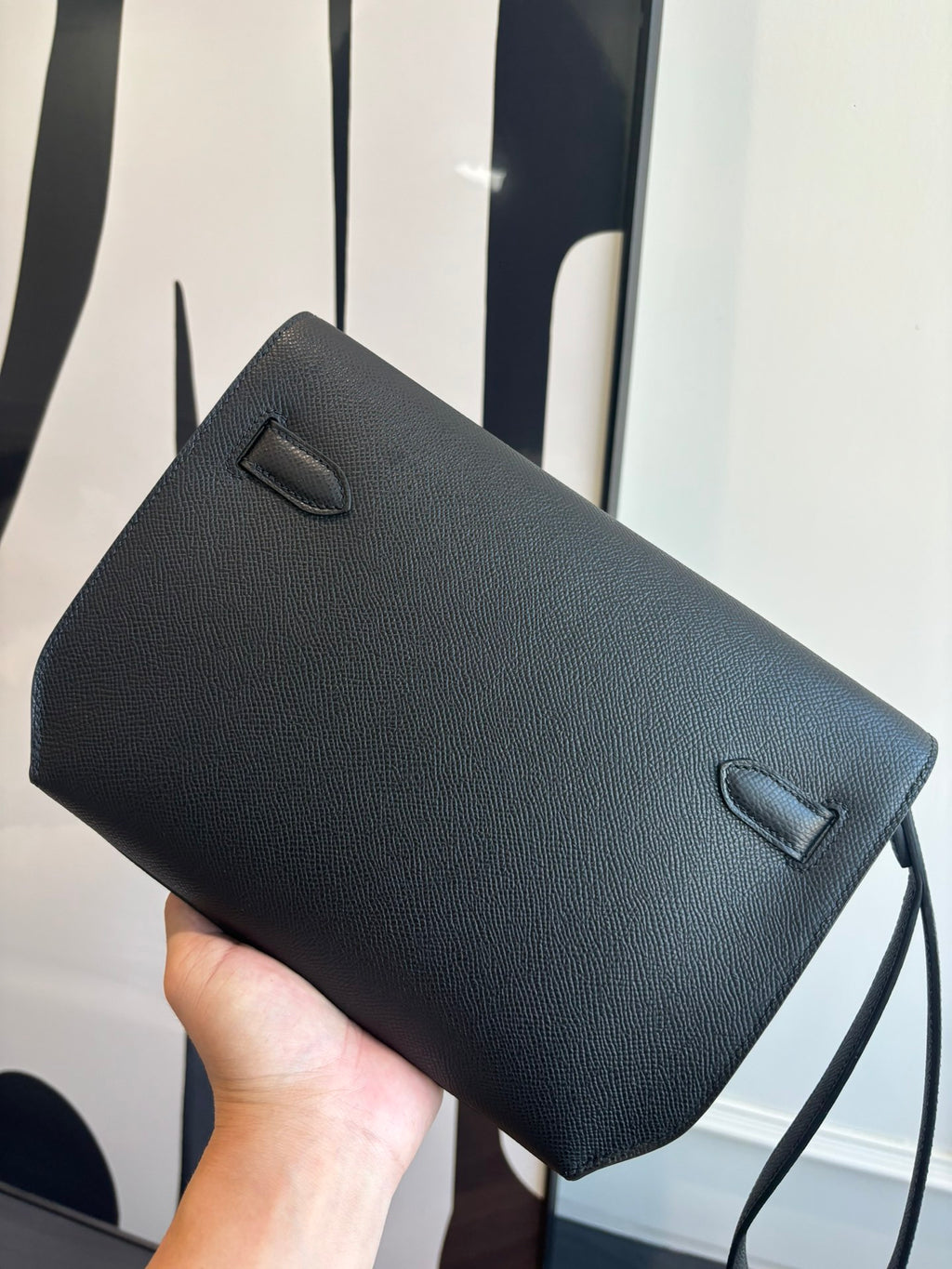 Hermes bag side view with flap closure, textured dark leather and slim strap loop