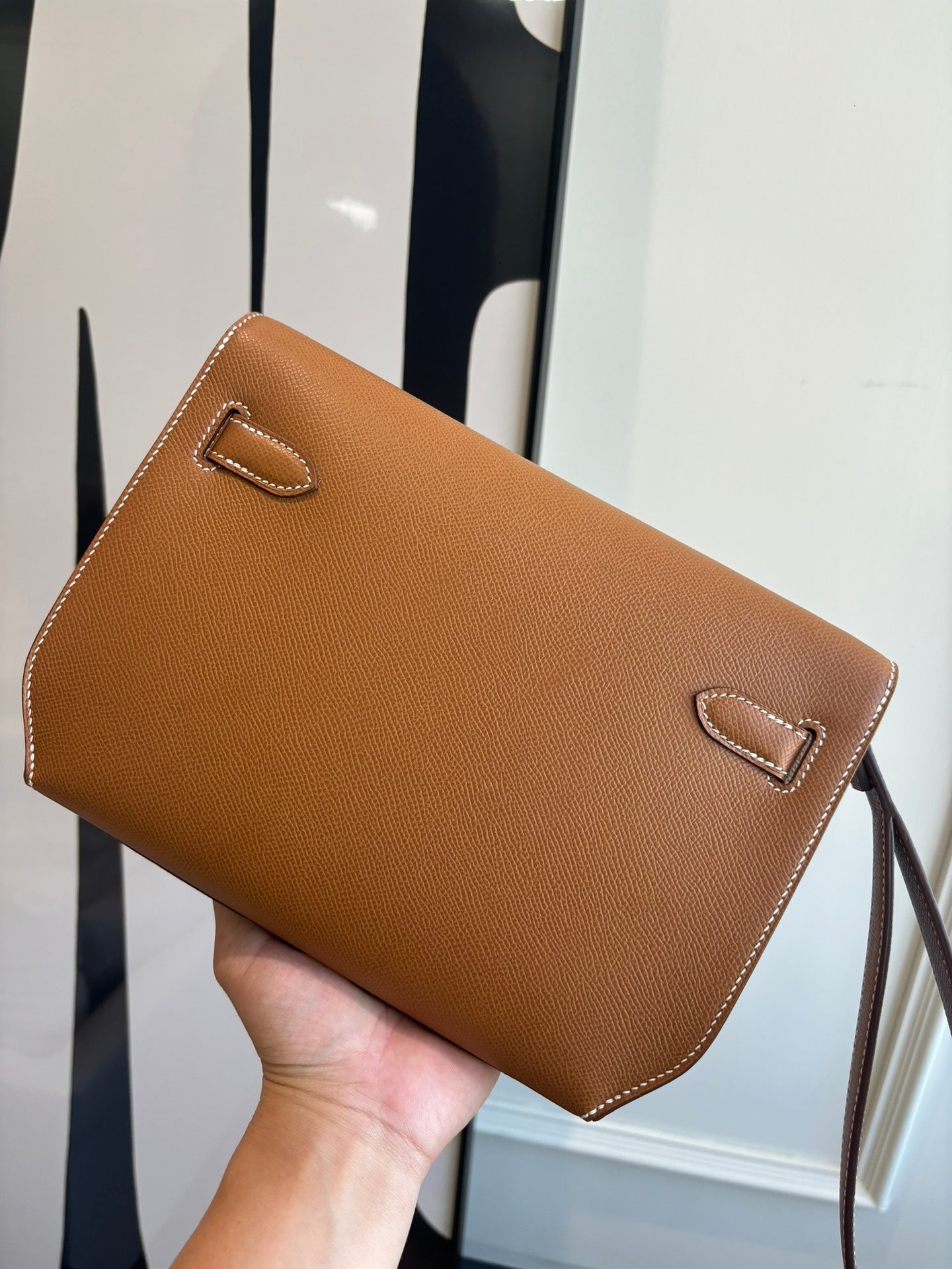 Brown leather flap bag front with stitched flap edge and small emblem detail