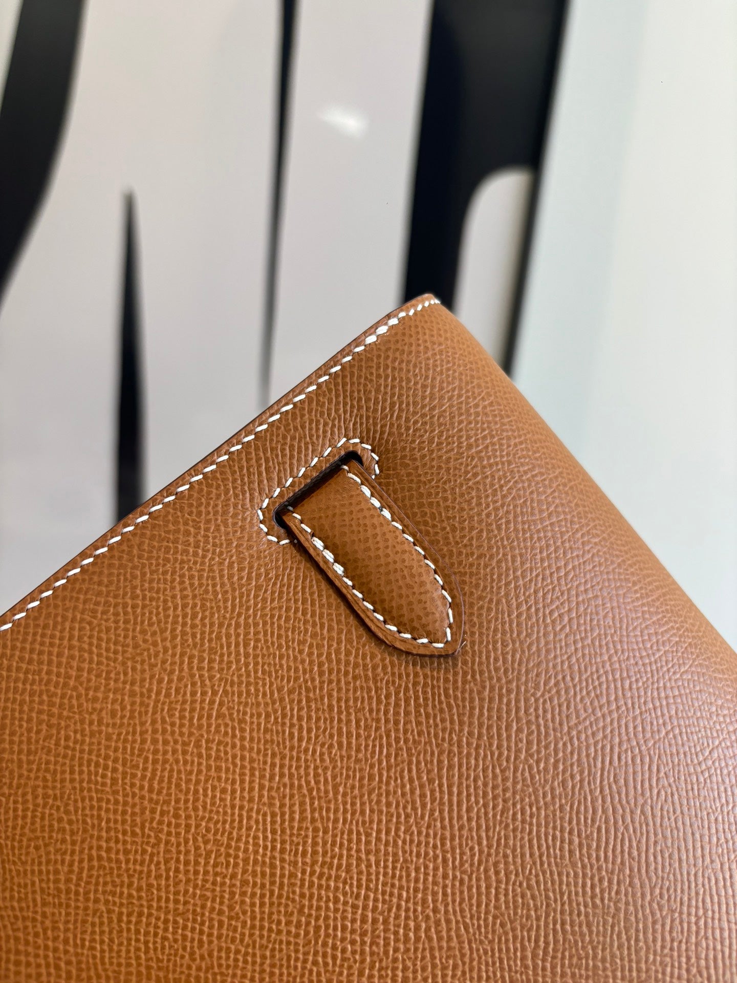 Brown leather flap bag corner detail with stitched tab and metal clasp