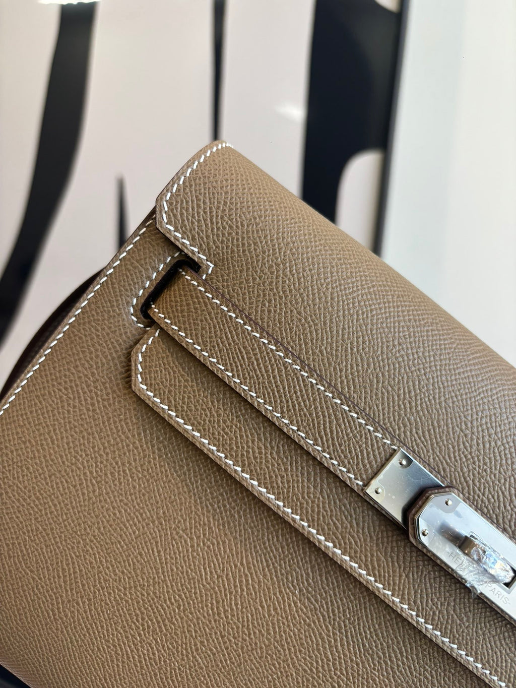 Hermes flap shoulder bag detail: silver-tone buckle and white edge stitching