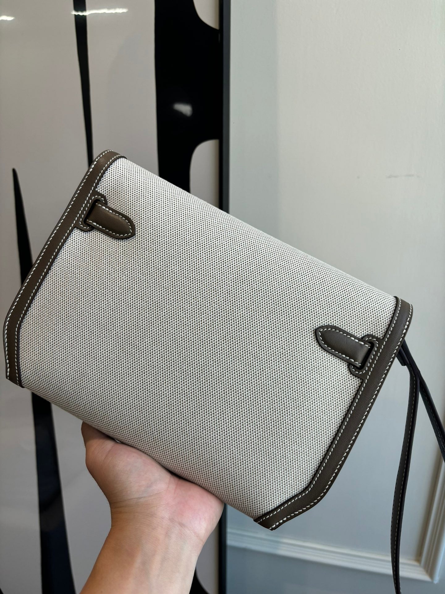 Beige textured Hermes bag with brown leather flap, front pocket, and shoulder strap
