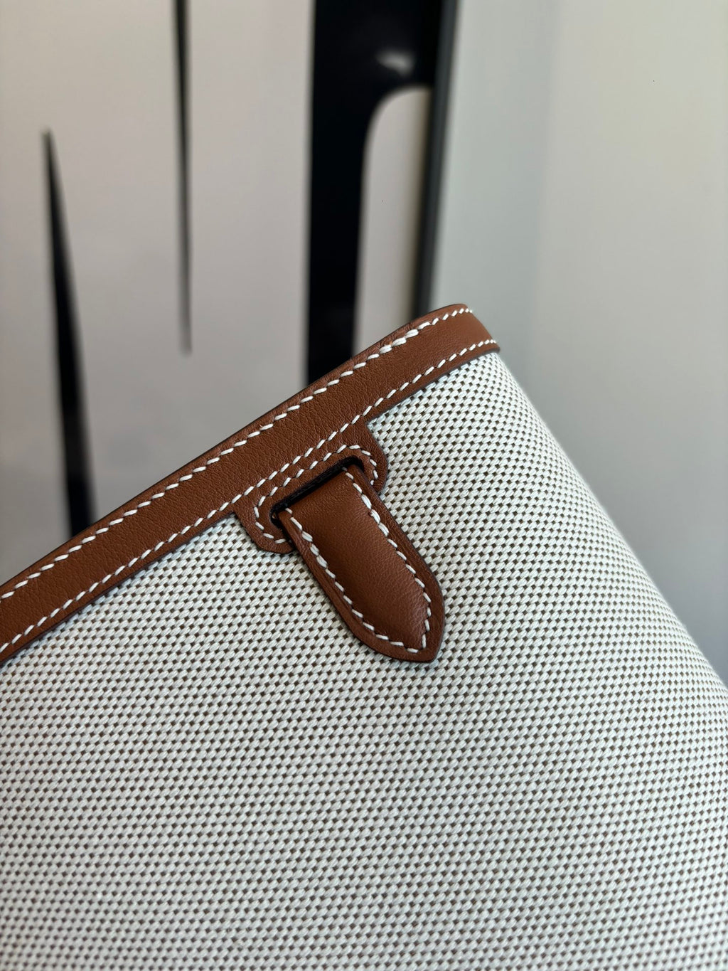 Hermes bag detail, brown leather snap tab on light textured canvas