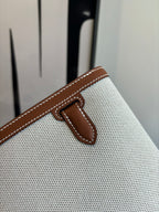 Hermes bag detail, brown leather snap tab on light textured canvas