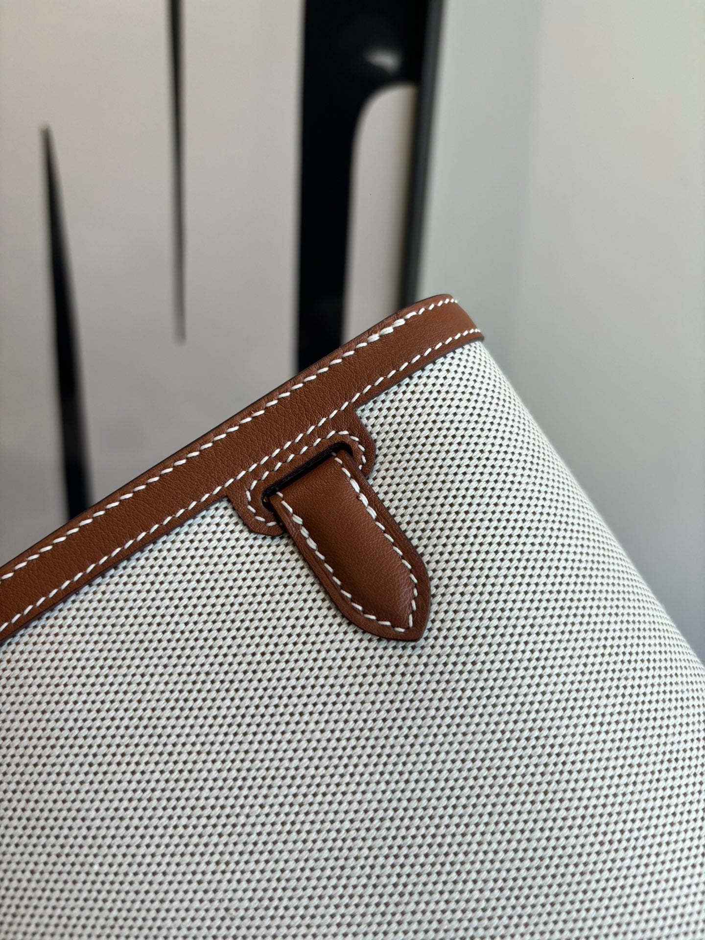 Hermes bag detail, brown leather snap tab on light textured canvas