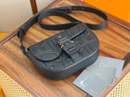 Dark crossbody bag with top handle and long strap, front buckle and flap