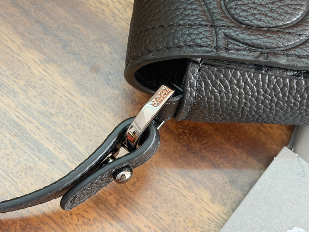 Side of dark crossbody bag with metal clasp and attached strap hardware