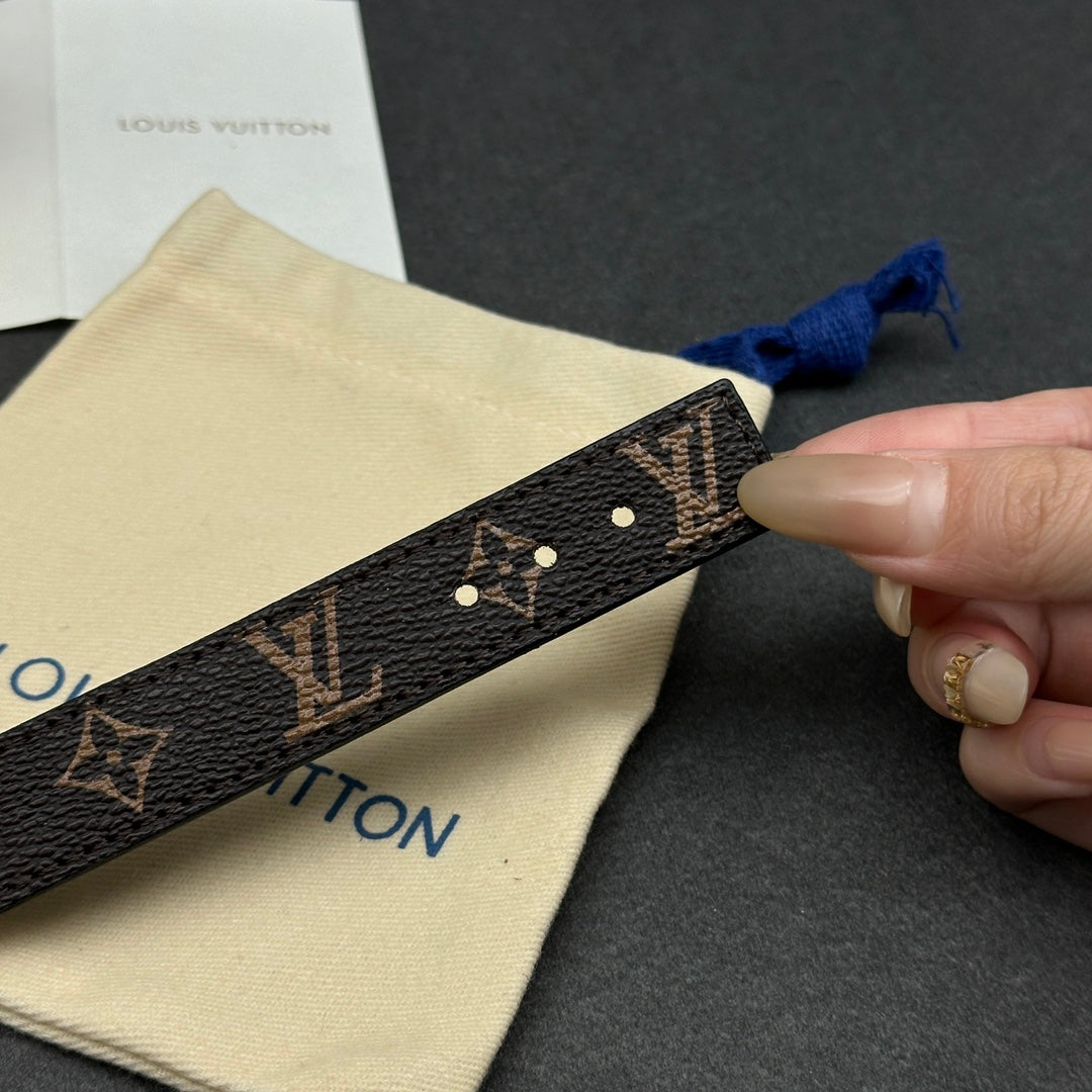 Louis Vuitton monogram strap with metal studs, held by a hand near the blue bow