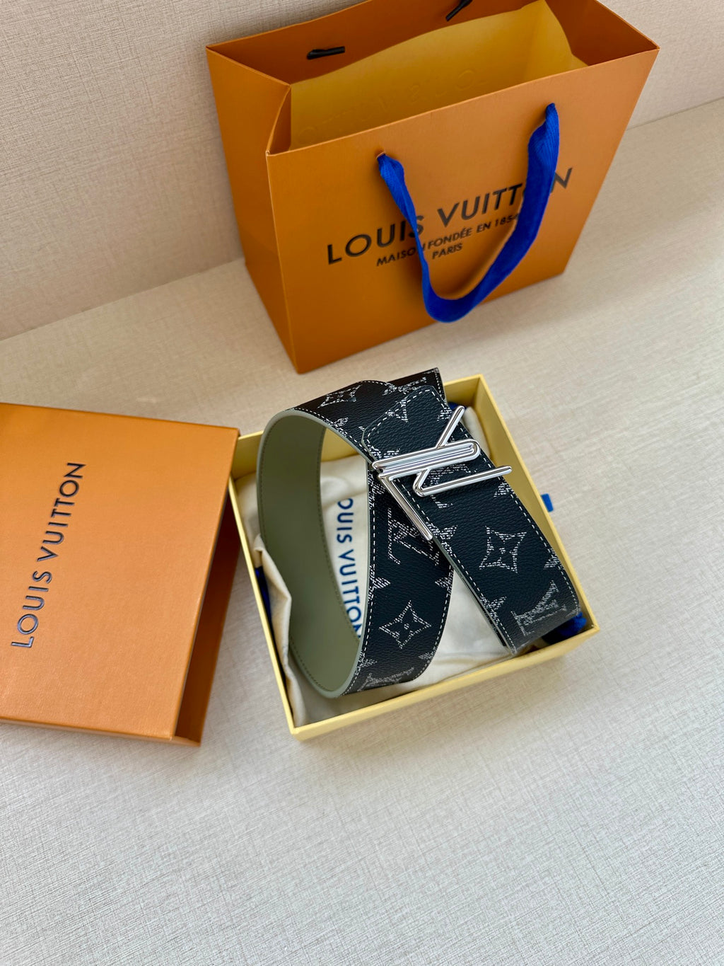 Louis Vuitton belt with dark navy monogram strap, gold-tone buckle, green underside.