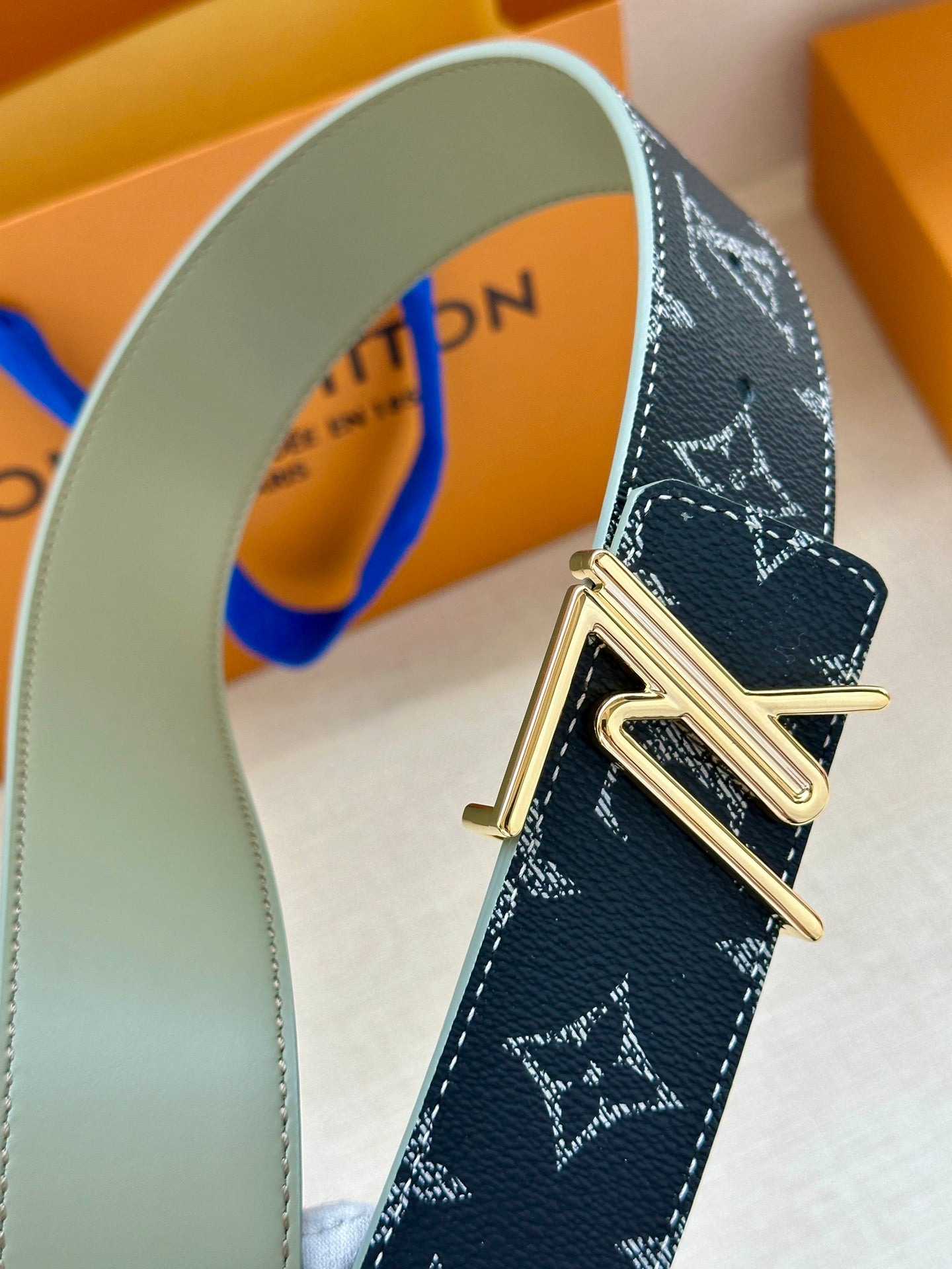Louis Vuitton belt close-up: dark navy monogram strap with gold-tone metal buckle.