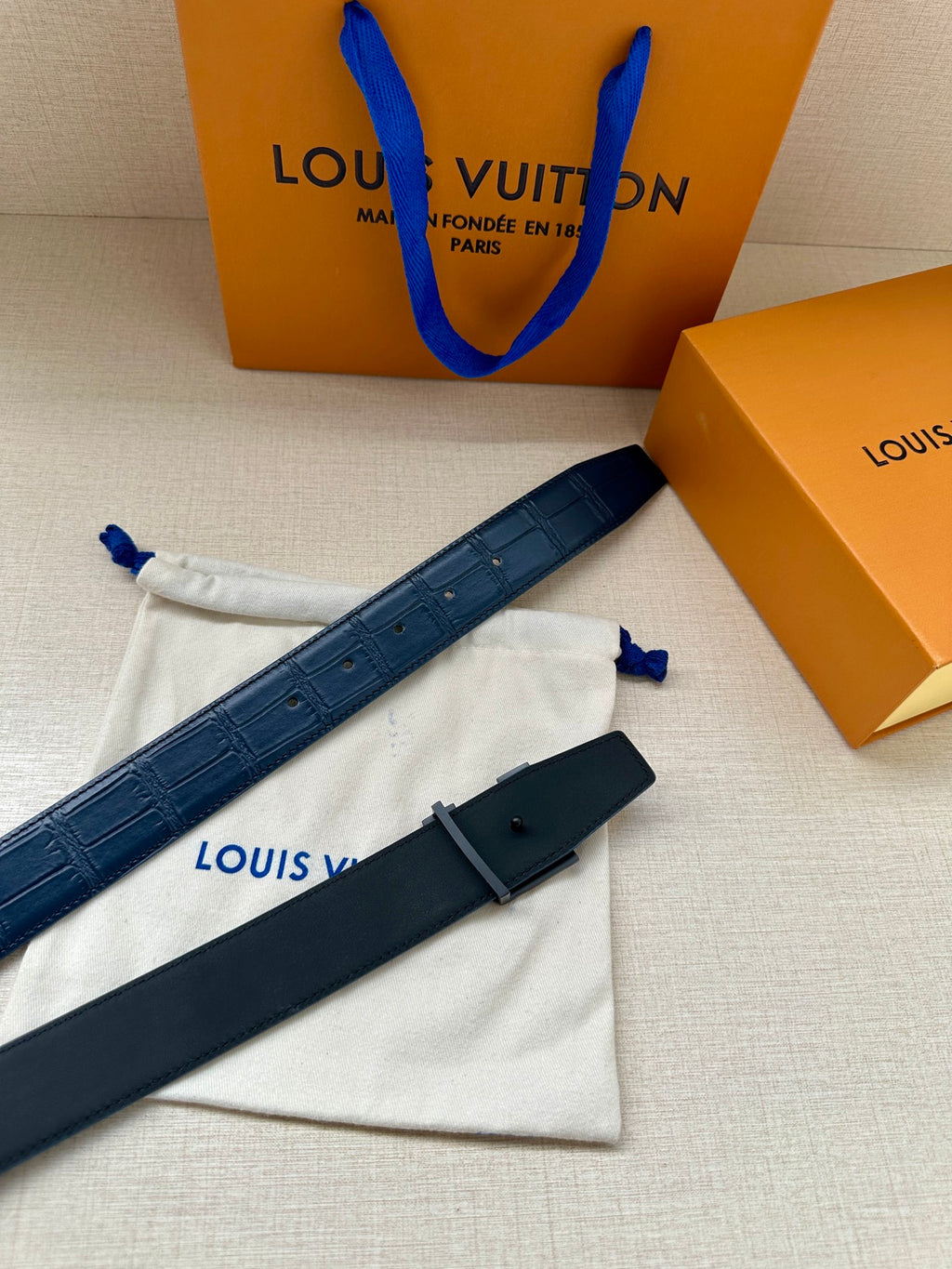 Louis Vuitton belt, dark blue strap with silver LV buckle, belt tail visible