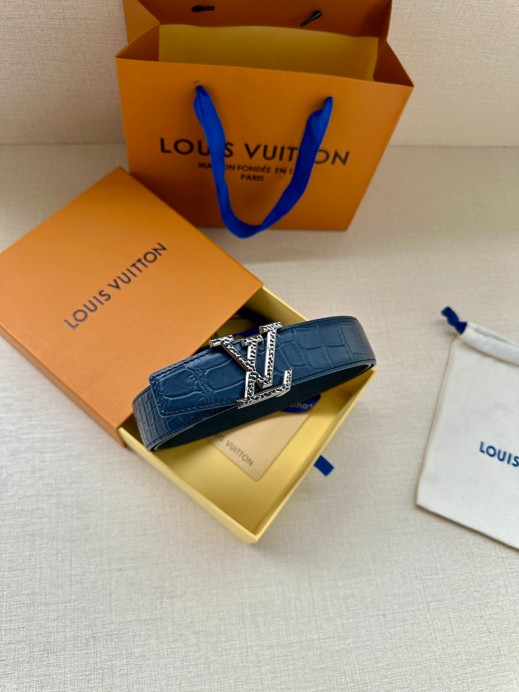 Blue leather belt with gold buckle, arranged beside a paper shopping bag