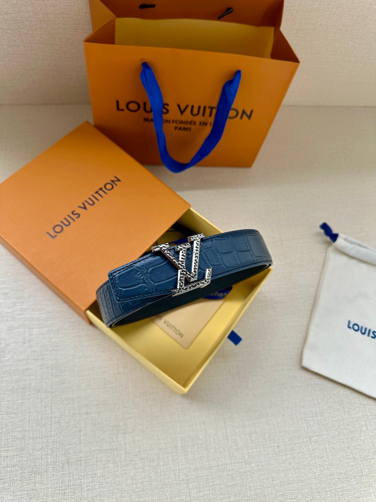 Blue leather belt with gold buckle, arranged beside a paper shopping bag