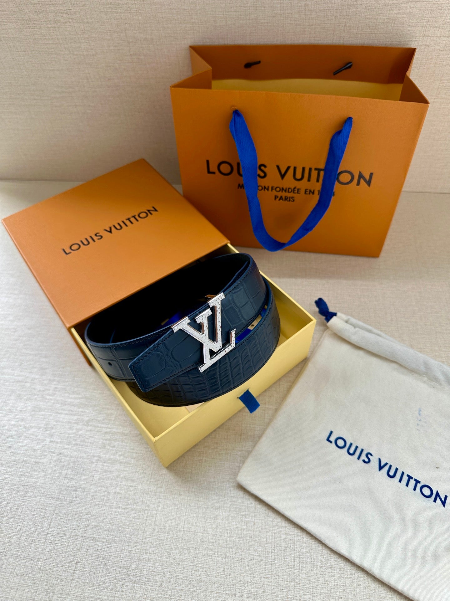 Blue leather belt with gold buckle, resting in a gift box with dust bag