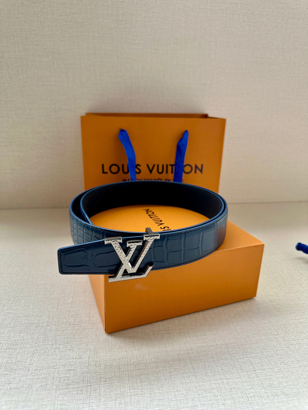 Blue leather belt with gold LV-style buckle, placed on a gift box