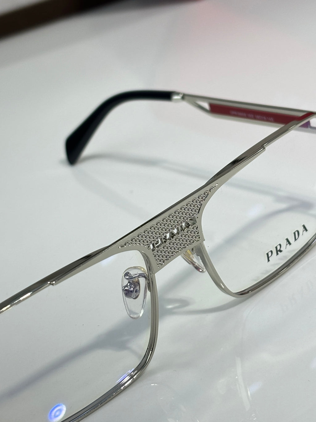 Prada eyeglasses close-up: silver frame with black temple tips, clear lenses