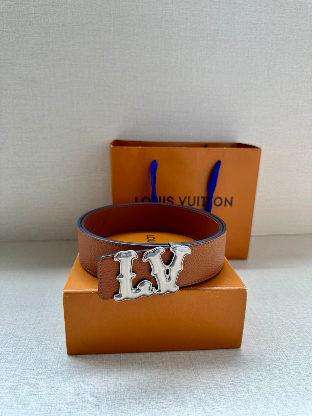 Tan leather belt with silver-toned LV buckle placed on an orange box