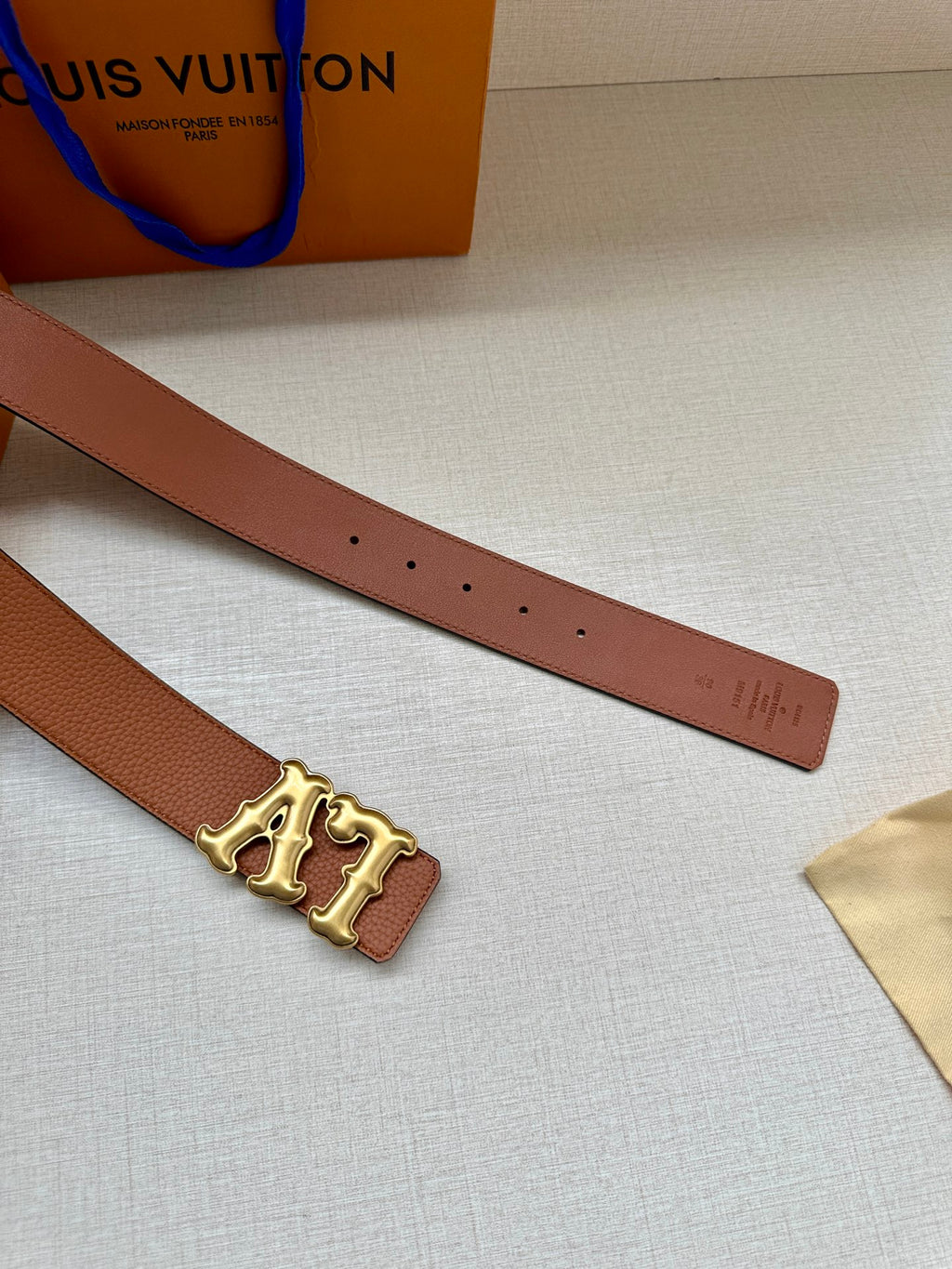 Tan leather belt with gold-toned LV buckle and row of punched holes