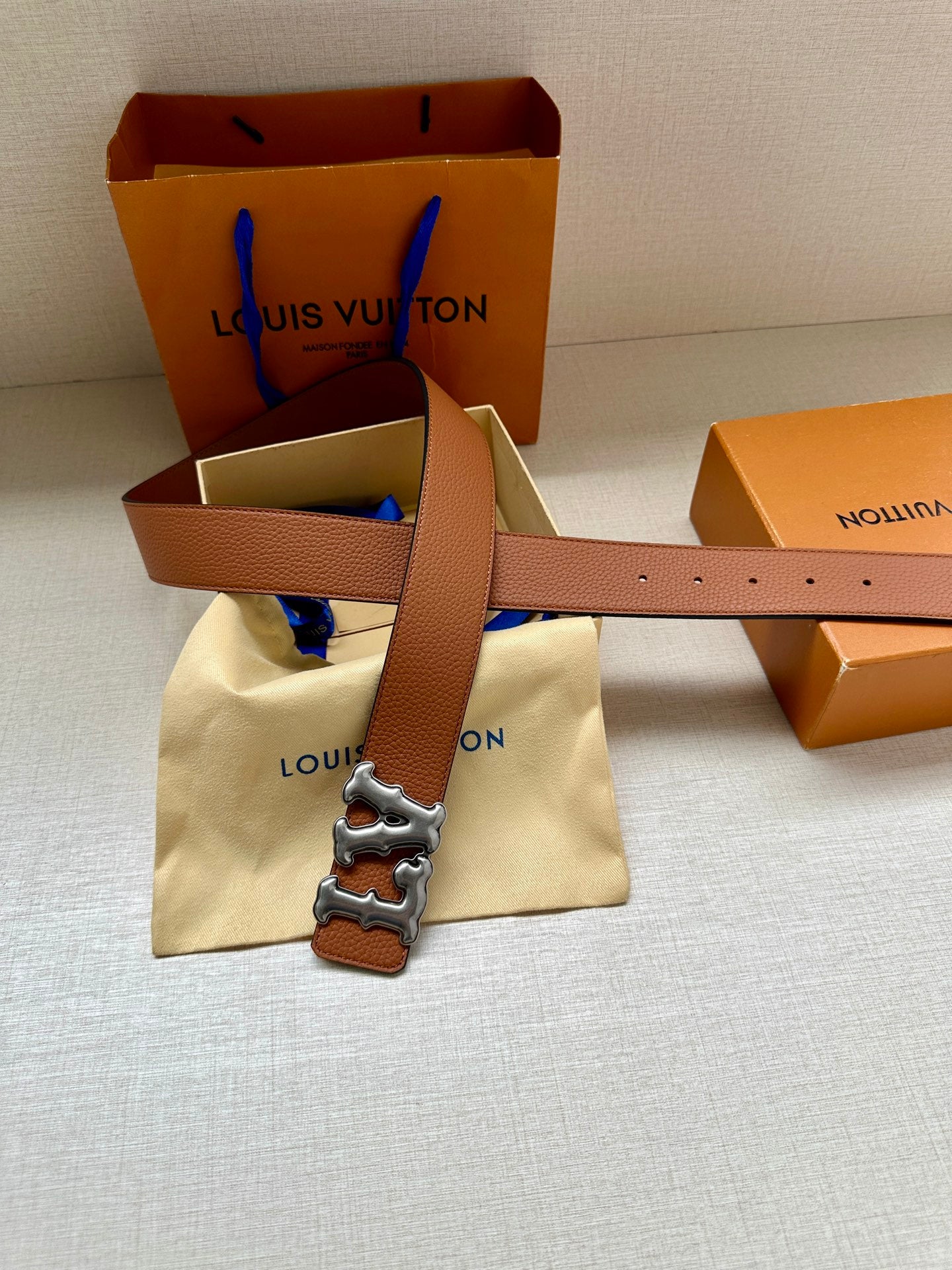 Tan leather belt with silver-toned LV buckle on a folded dust bag