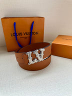 Tan leather belt with silver-toned LV buckle, belt looped on the bed