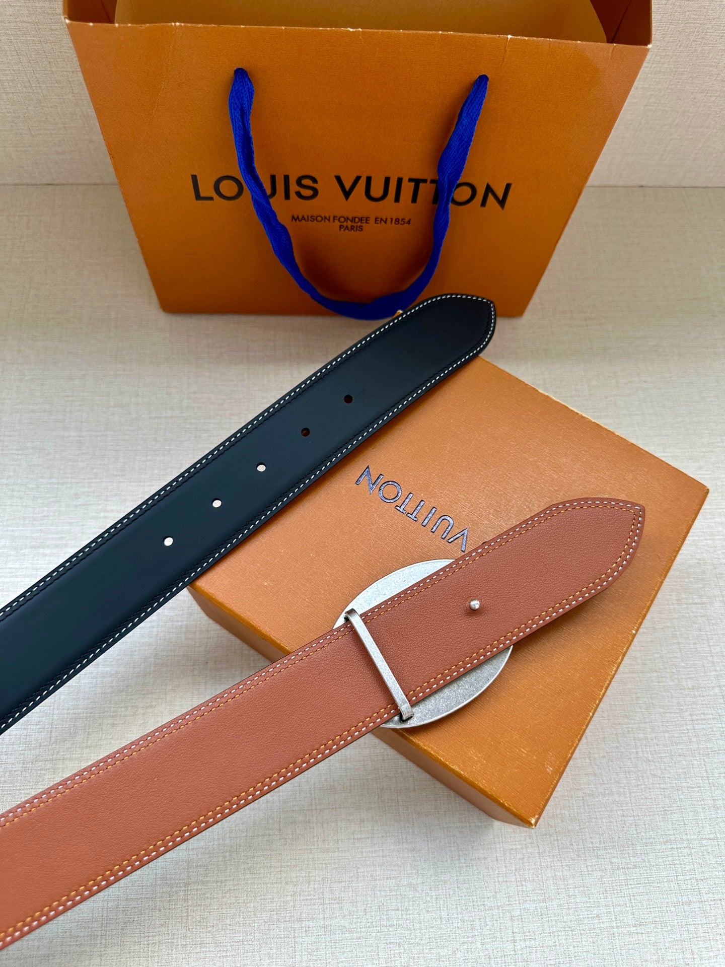 Navy and tan leather belt with silver buckle and rows of punched holes