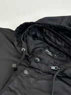Black parka jacket close-up with brand patch, snap buttons, and drawcord