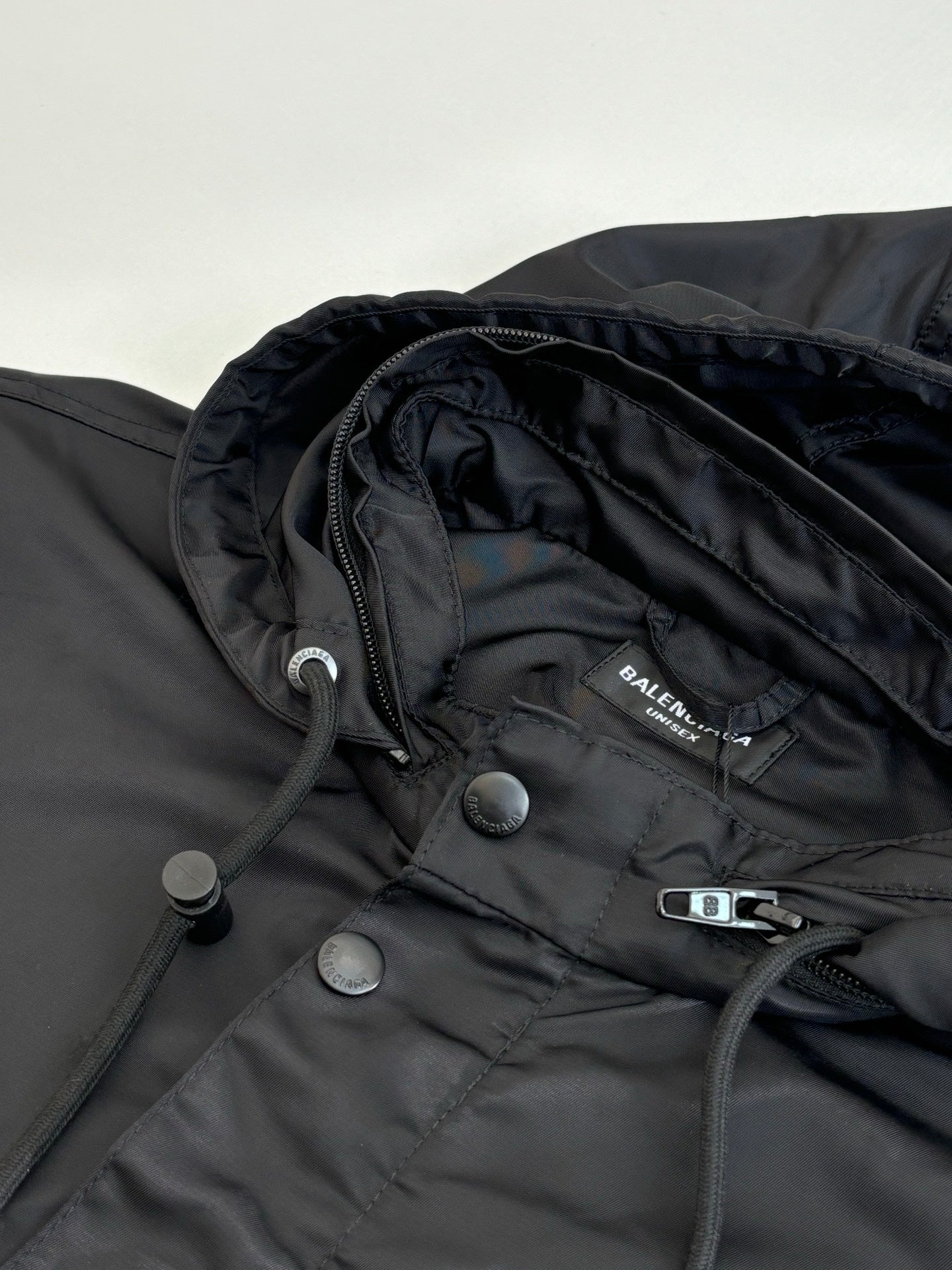 Black parka jacket close-up with brand patch, snap buttons, and drawcord