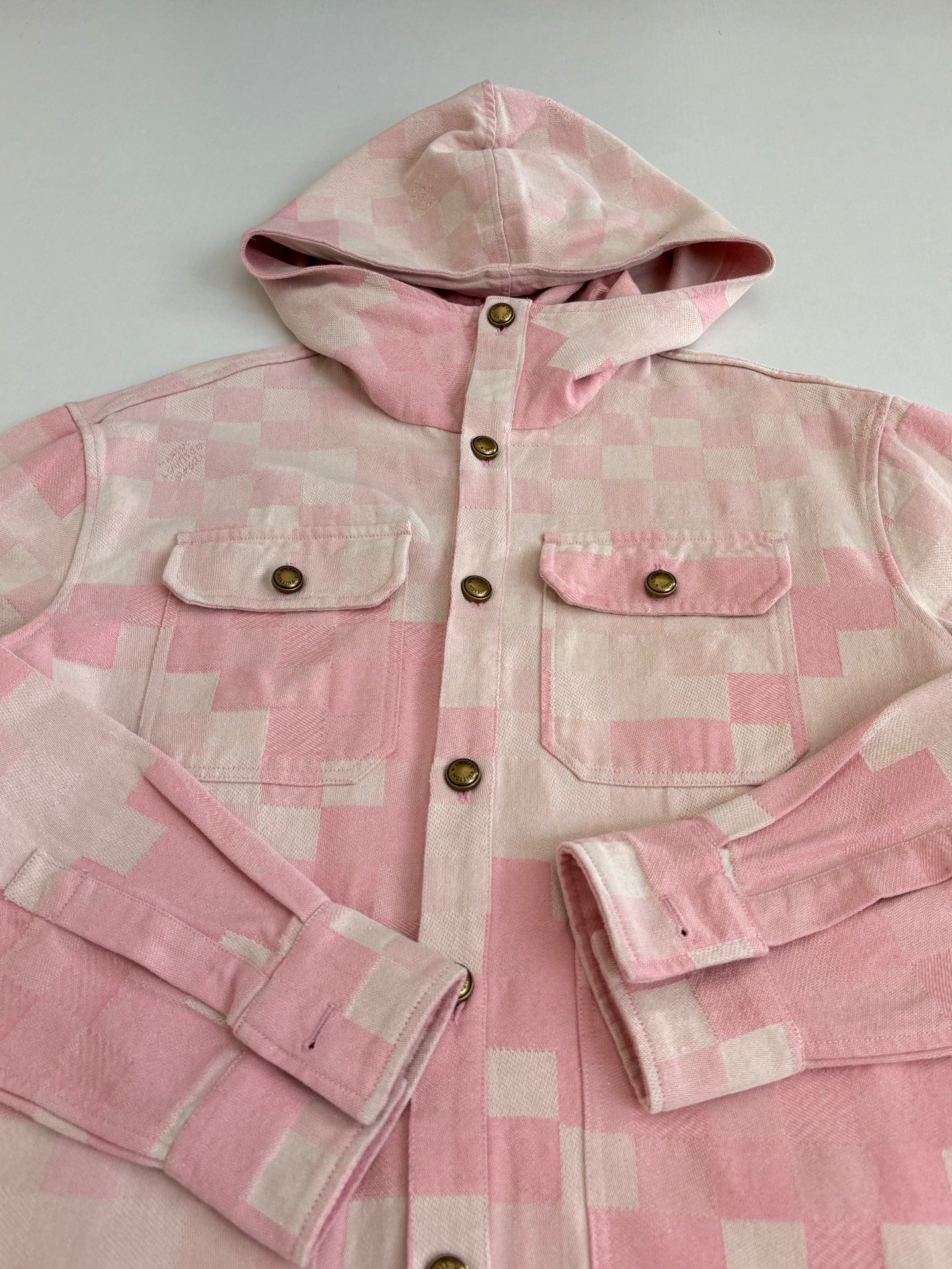 Pink hooded jacket close-up with chest pockets, gold buttons, and patchwork check pattern