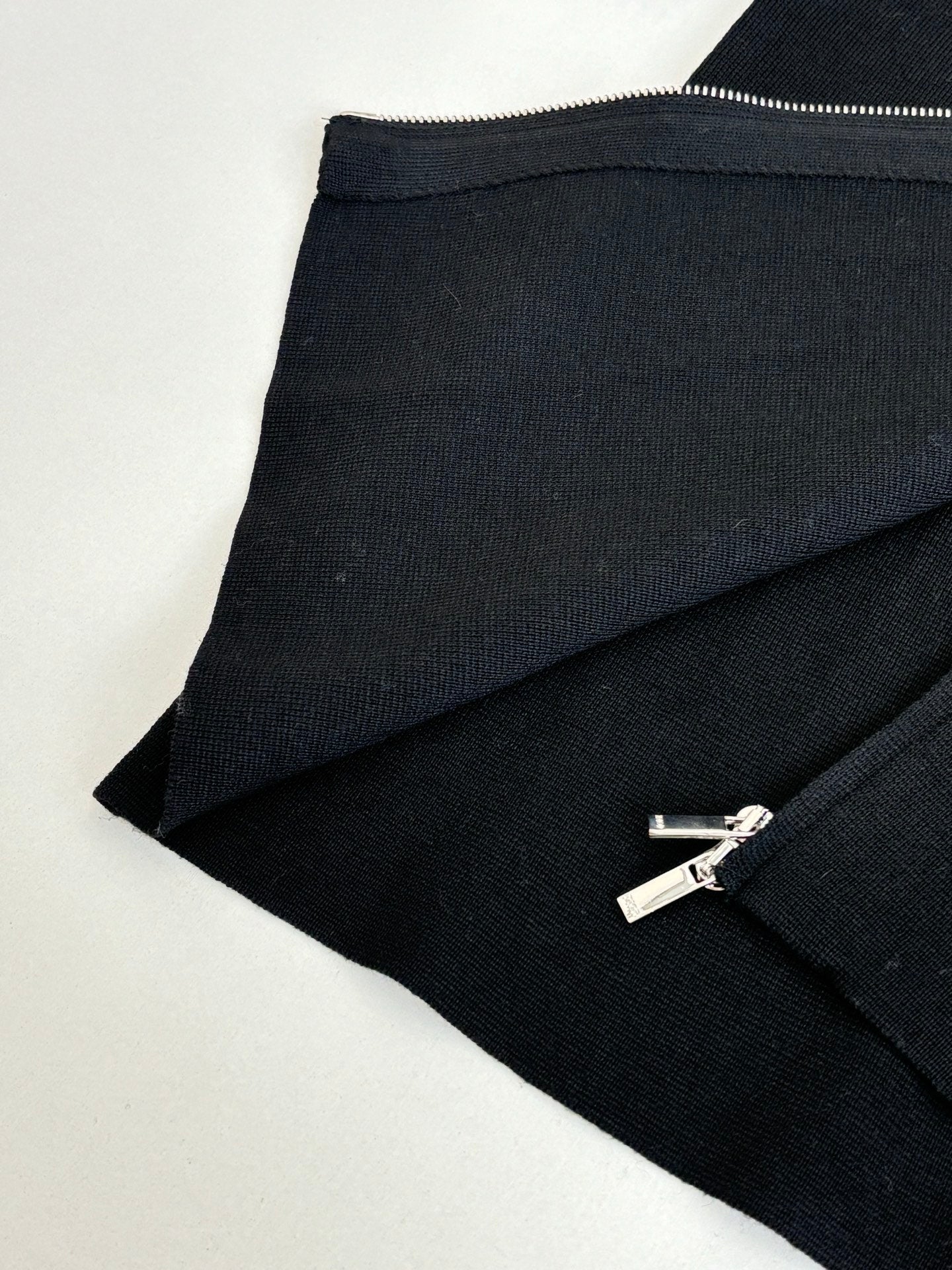 Black zip jacket hem and zipper with silver pull, angled close-up