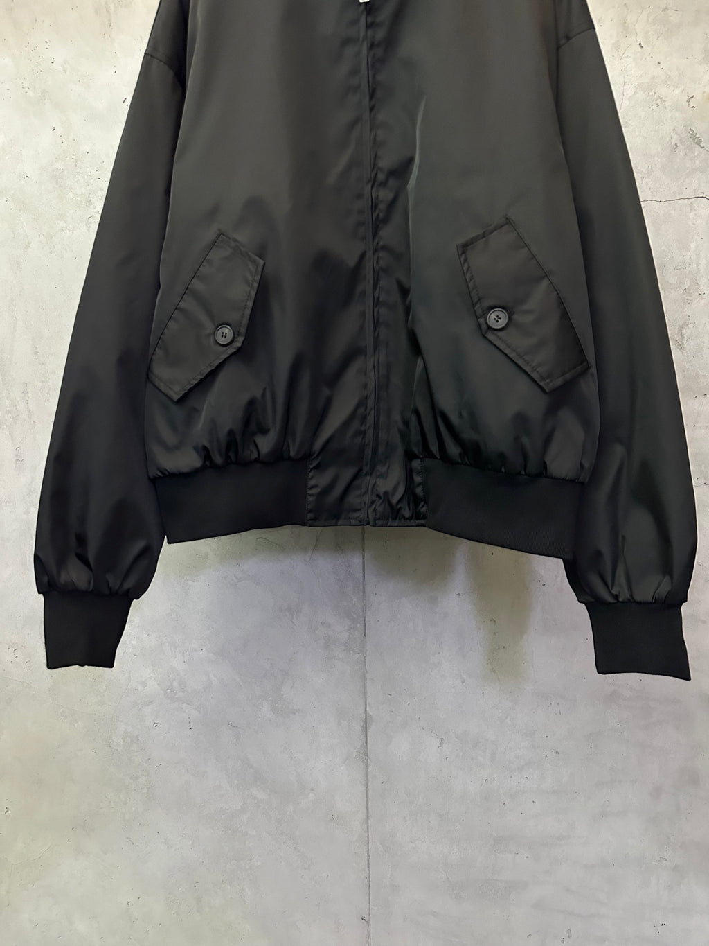 Black bomber jacket showing flap pockets and ribbed cuffs at the hemline