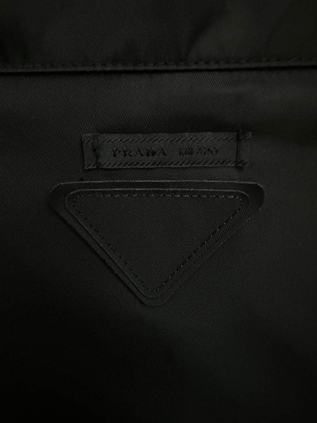 Triangular PRADA logo label on black jacket fabric