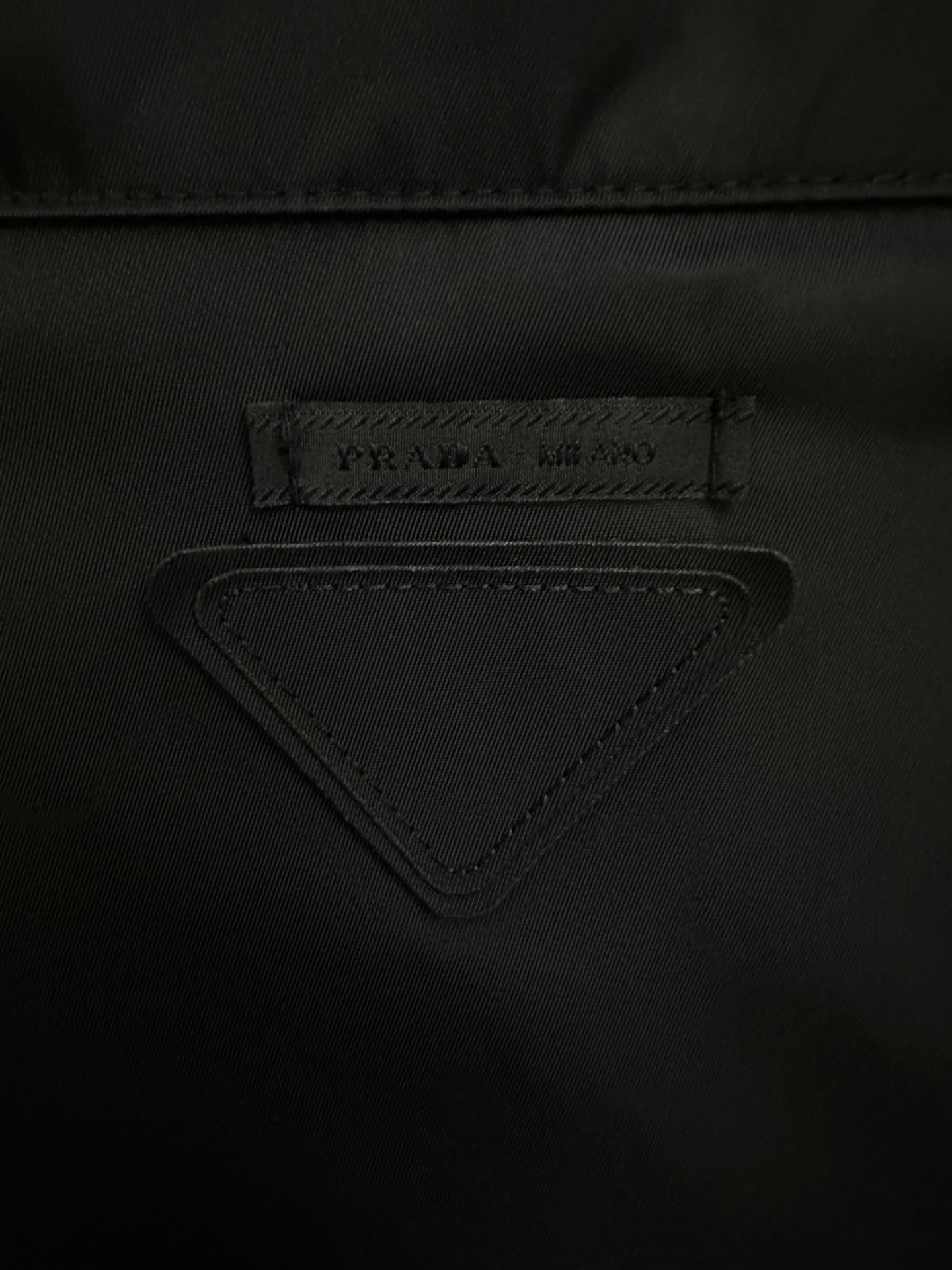 Triangular PRADA logo label on black jacket fabric