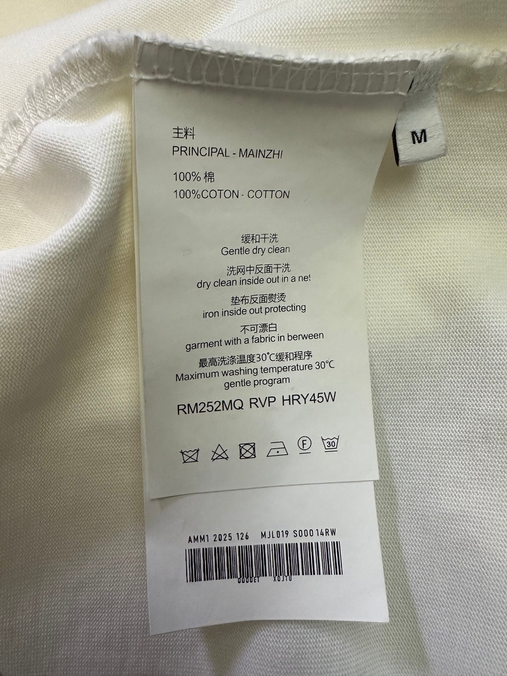 Cotton T-shirt care label on cream fabric, size M, 100% cotton
