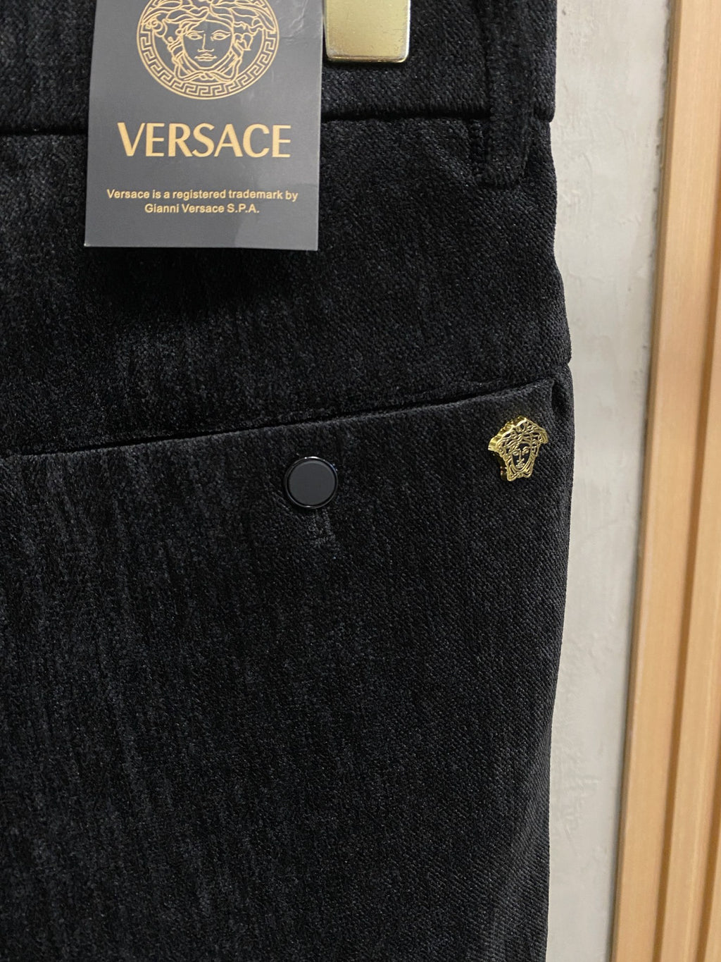 Black Versace trousers with gold logo accent on pocket and round button