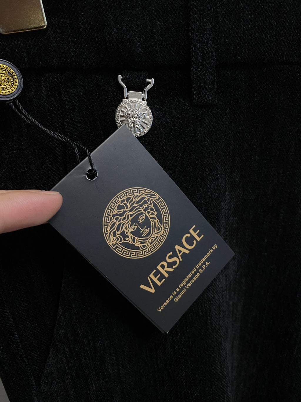 Black Versace trousers with attached hang tag showing logo
