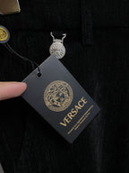 Black Versace trousers with hanging tag and coin charm detail