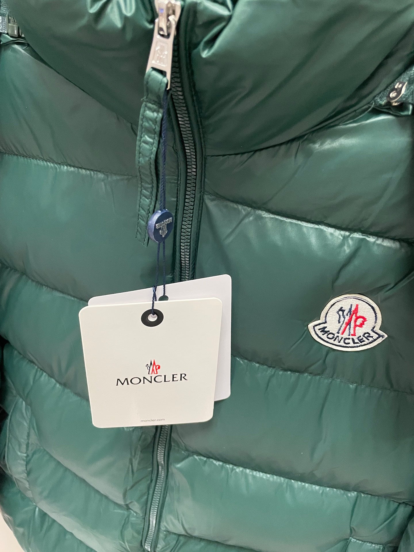 Dark green puffer jacket close-up with front zipper and circular logo patch
