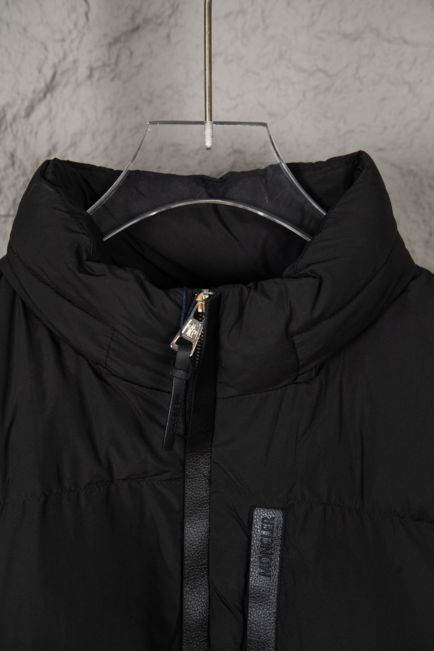 Long black puffer jacket front with stand collar, zipper pull, and inner logo patch