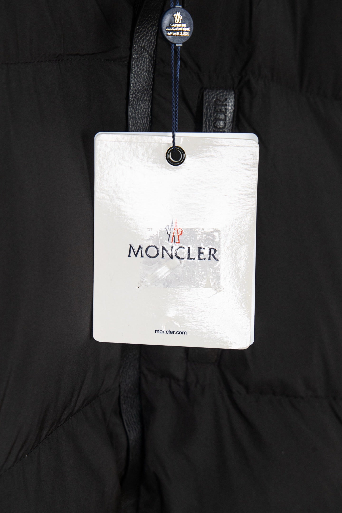 Long black puffer jacket with brand hang tag labeled MONCLER