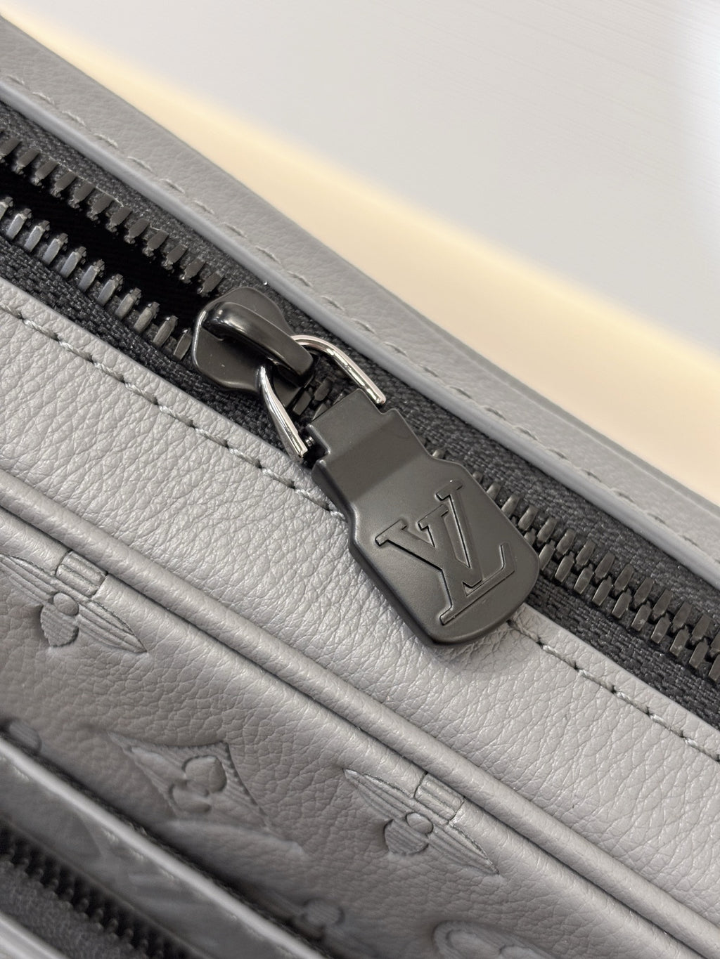 Louis Vuitton gray bag close-up of zipper pull and logo-stamped metal hardware
