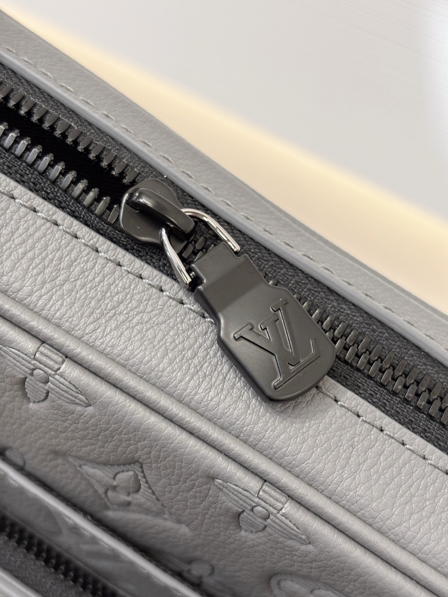 Louis Vuitton gray bag close-up of zipper pull and logo-stamped metal hardware