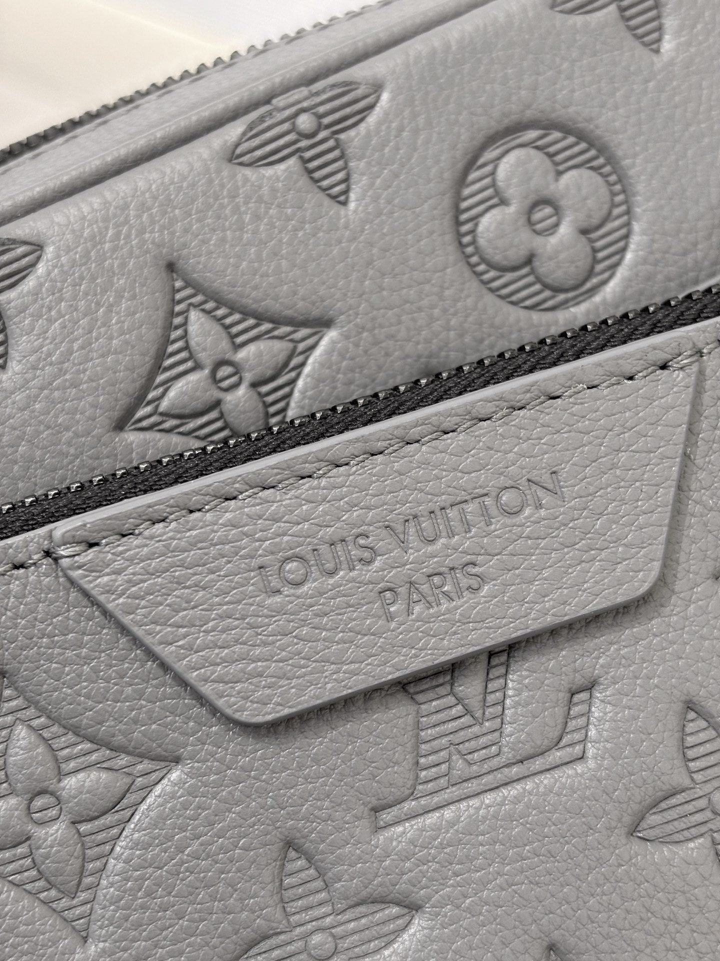 Louis Vuitton gray leather bag close-up with embossed monogram pattern and zipper trim